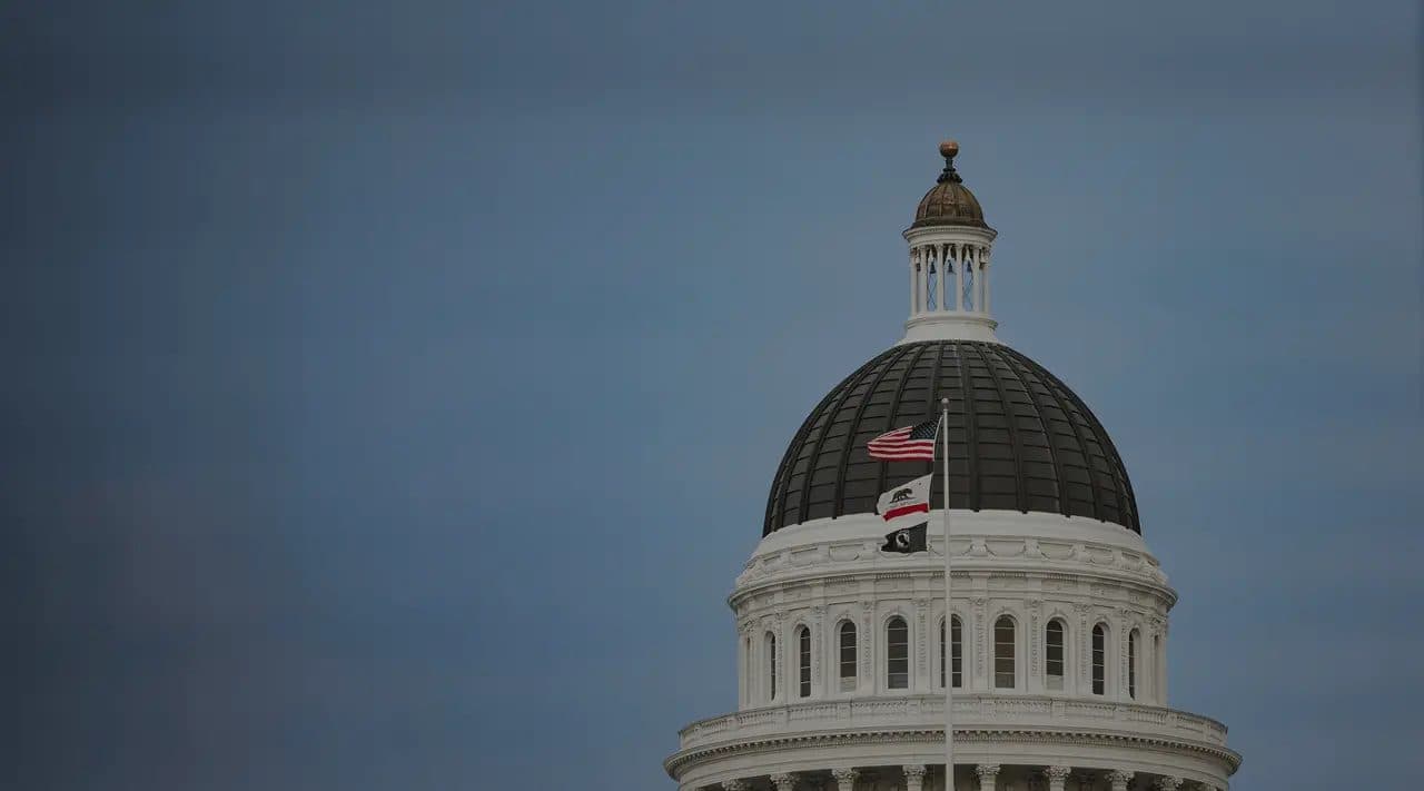 The dome of the California State Capitol in Sacramento against a clear sky, with flags flying