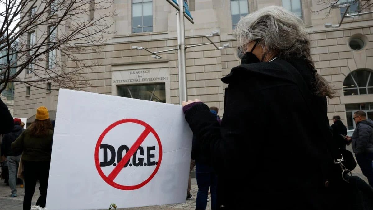Un manifestant tient une pancarte avec « DOGE » barré devant un bâtiment du gouvernement américain