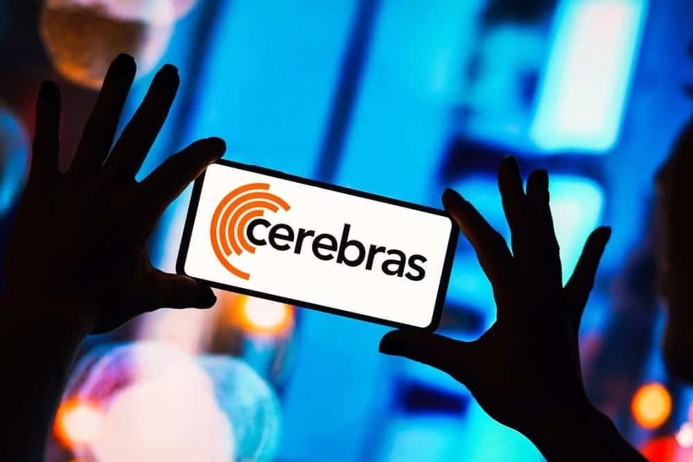 Un smartphone que muestra el logotipo de Cerebras, sostenido por unas manos en silueta contra una luz azul.