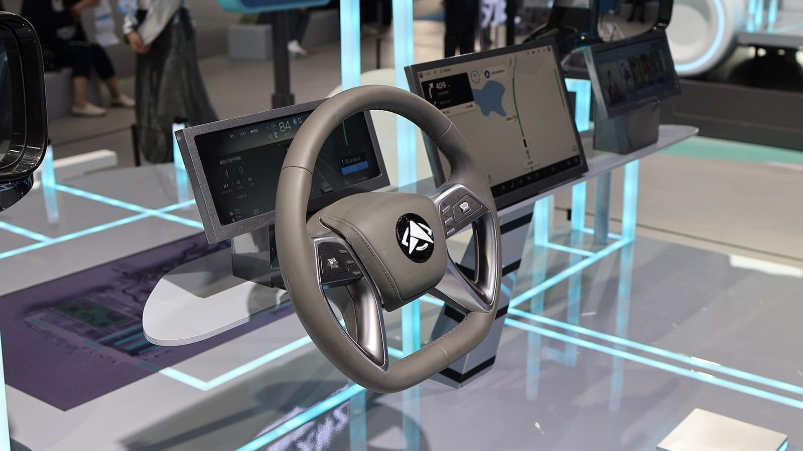 A car cockpit mock-up with a steering wheel and curved instrument displays on a lit exhibition stand.