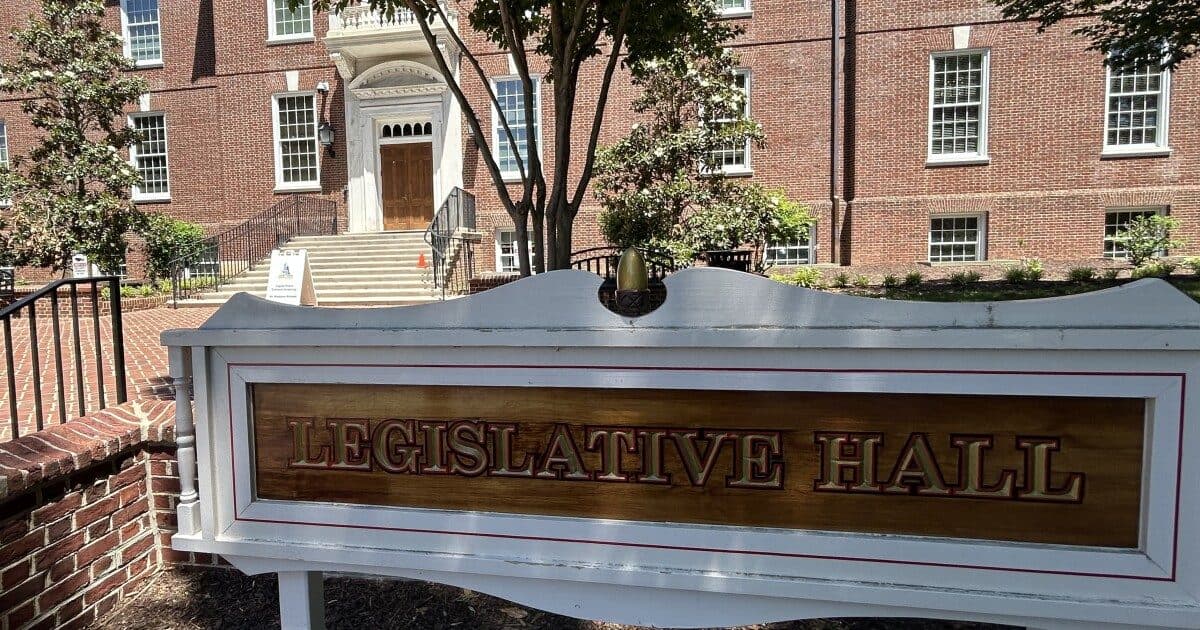 A placa gravada com a inscrição 'Legislative Hall' do lado de fora do capitólio estadual de Delaware, em Dover, com o prédio de tijolos e árvores ao fundo.