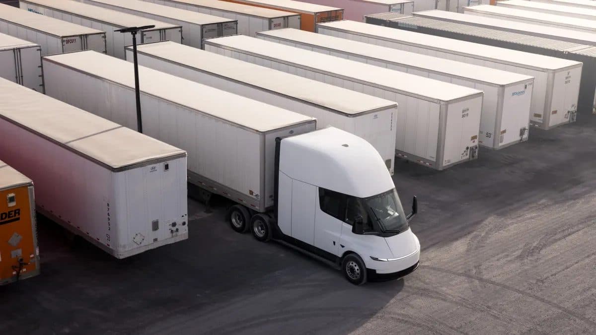 A white Tesla Semi tractor unit parked in a freight yard alongside rows of white trailers