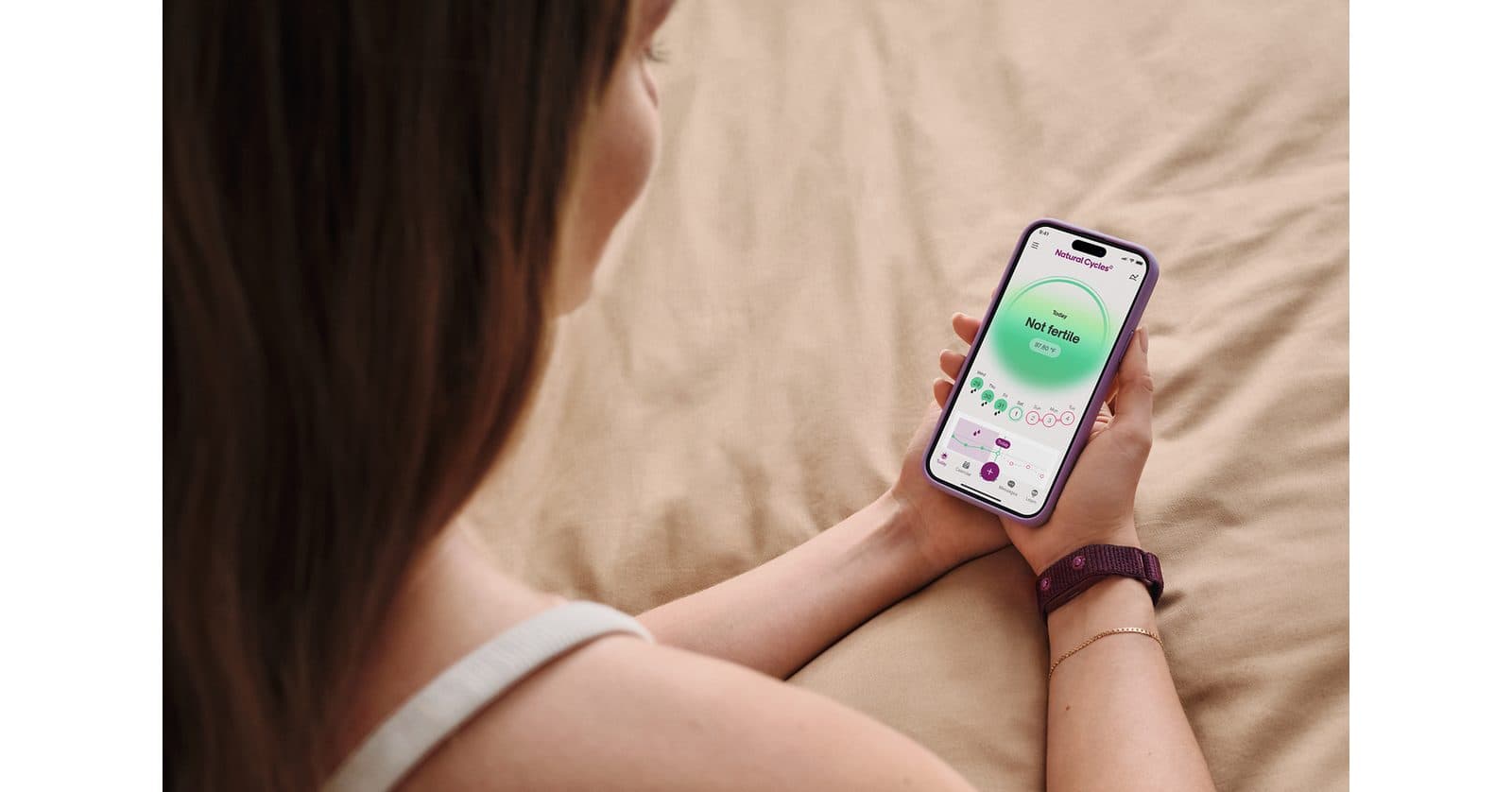 A person lying down and holding a smartphone in both hands, a cycle-tracking app open on the screen