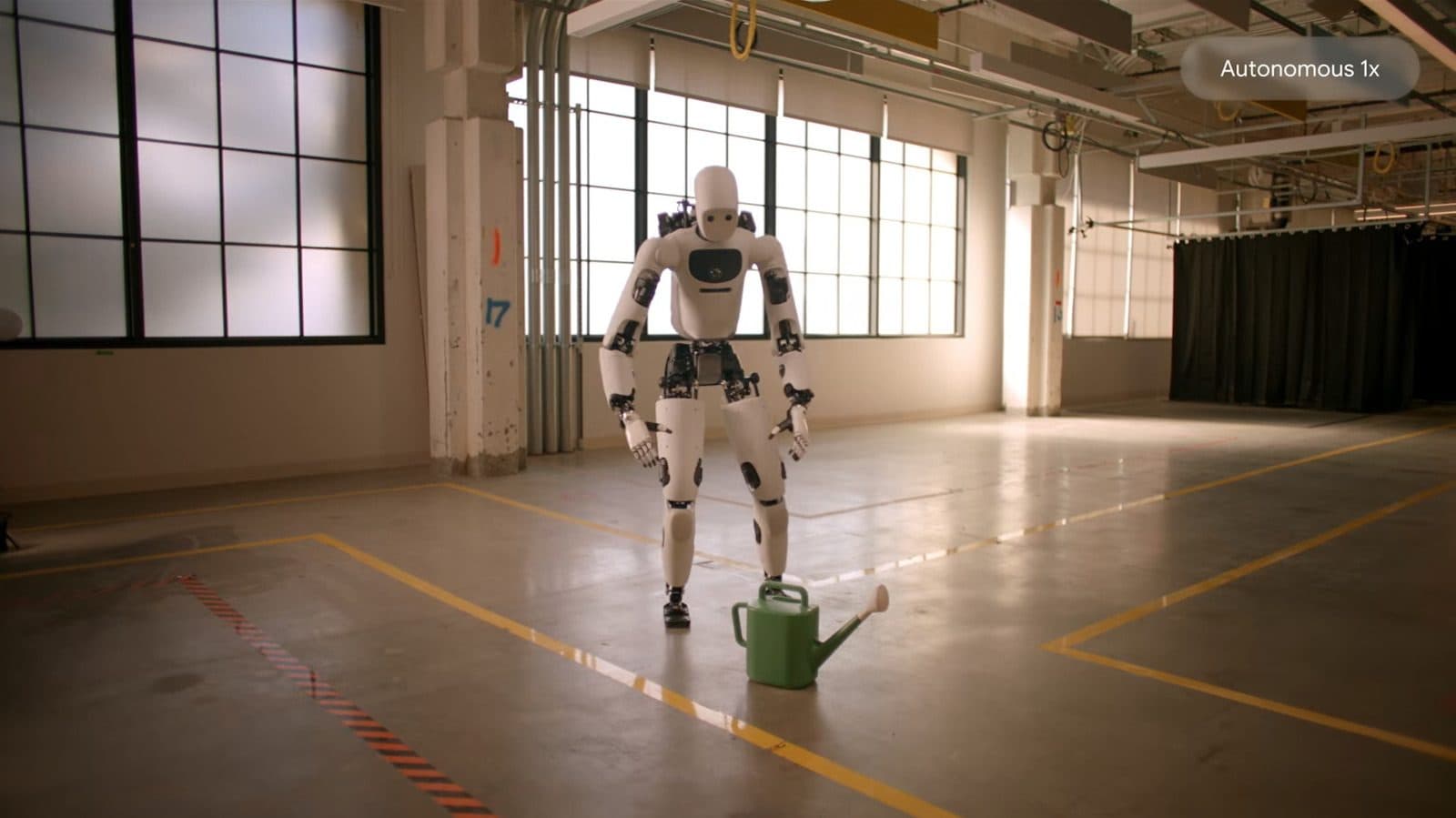 Un robot umanoide trasporta un annaffiatoio su un pavimento di magazzino vuoto, nel filmato indicato come autonomo a velocità 1x.