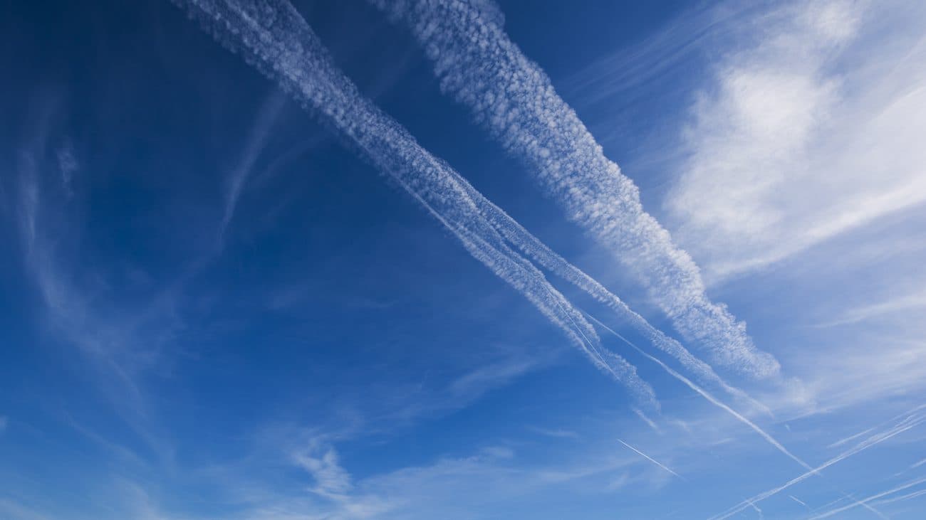 Aircraft contrails streaking diagonally across a blue sky with thin cirrus cloud.