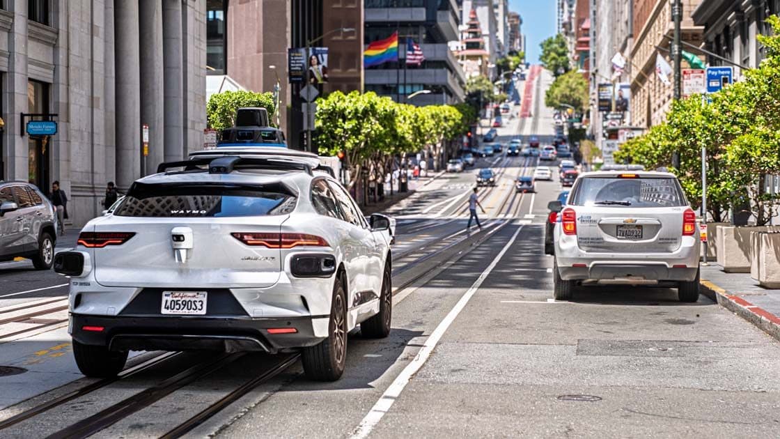 Un véhicule Waymo blanc équipé de capteurs sur le toit roulant dans une rue de San Francisco