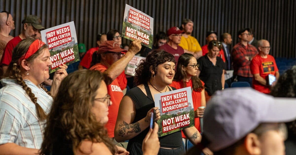 Des habitants lors d'une réunion publique tenant des pancartes imprimées portant les mentions « Indy needs a data center moratorium » et « Not weak regulations ».