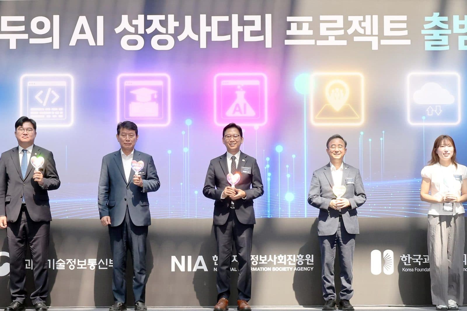Autoridades no palco durante a cerimônia de lançamento do projeto nacional de IA na Coreia, em frente a um banner em coreano e aos logotipos do ministério e da NIA