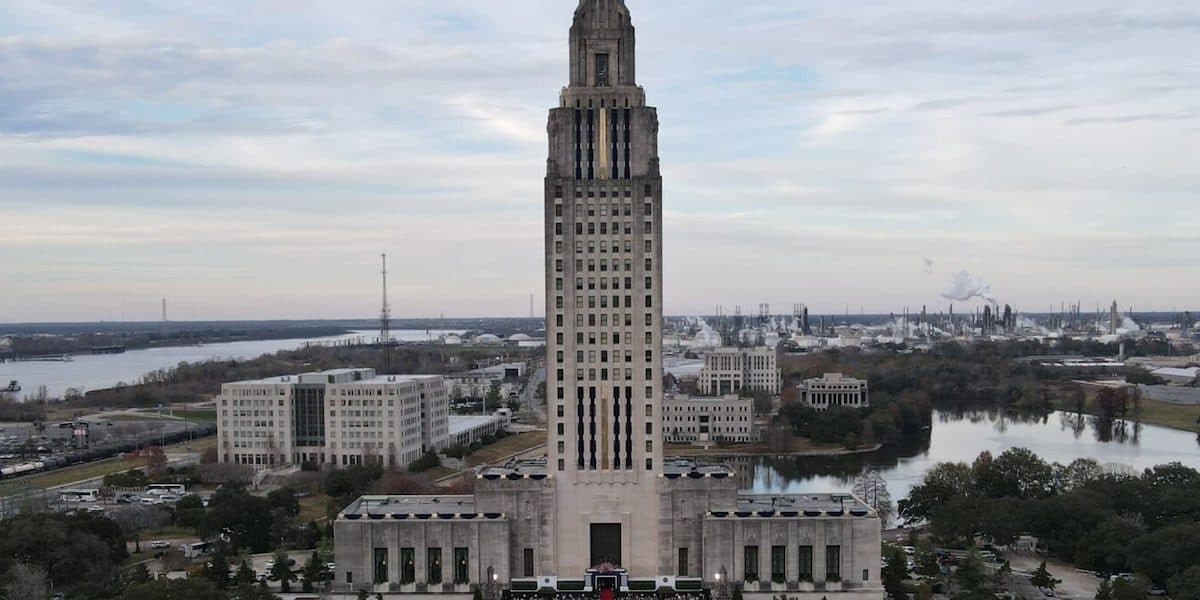 Vue aérienne de la tour du Capitole de l’État de Louisiane à Baton Rouge, avec le Mississippi et des cheminées de raffinerie au loin.