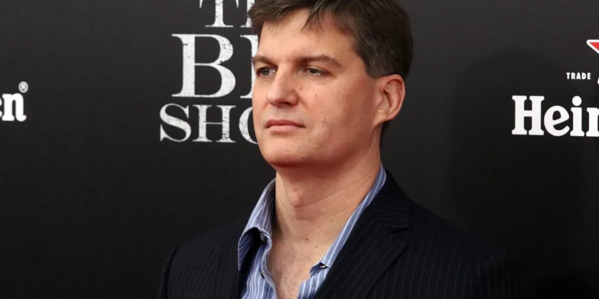 Investidor Michael Burry em um paletó listrado e camisa listrada aberta, fotografado diante de um painel com o título do filme The Big Short.