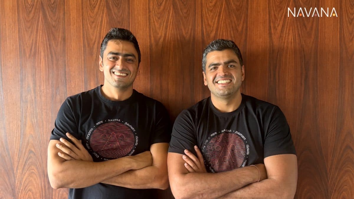 Navana.ai founders Raoul and Jai Nanavati stand with arms folded against a wood-panelled wall under the Navana wordmark.
