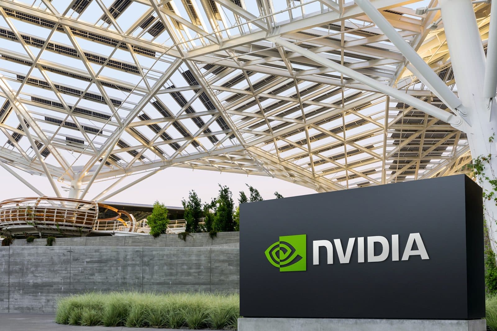 Логотип и надпись Nvidia на тёмной вывеске у штаб-квартиры компании, над которой виден белый стальной навес здания.