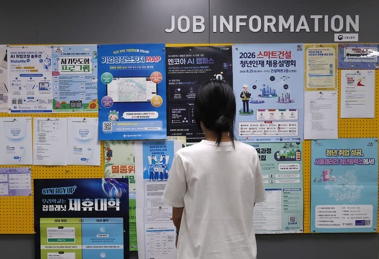 Une personne vue de dos lisant un panneau coréen d’information sur l’emploi intitulé JOB INFORMATION, couvert d’affiches de salons de l’emploi et de formation à l’IA