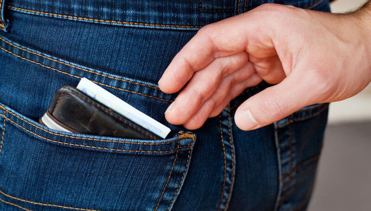 A close-up of a hand pulling a slim wallet from the back pocket of a pair of blue jeans.