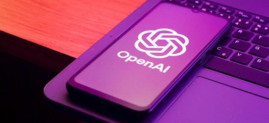 شعار وكلمة OpenAI ظاهران على شاشة هاتف ذكي يستقر على لوحة مفاتيح حاسوب محمول، بإضاءة بنفسجية.