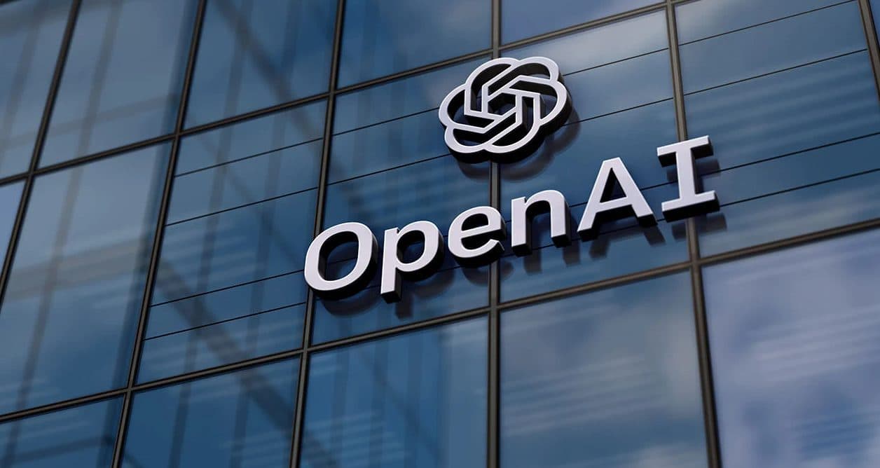 The OpenAI logo and wordmark mounted on a glass office building facade.