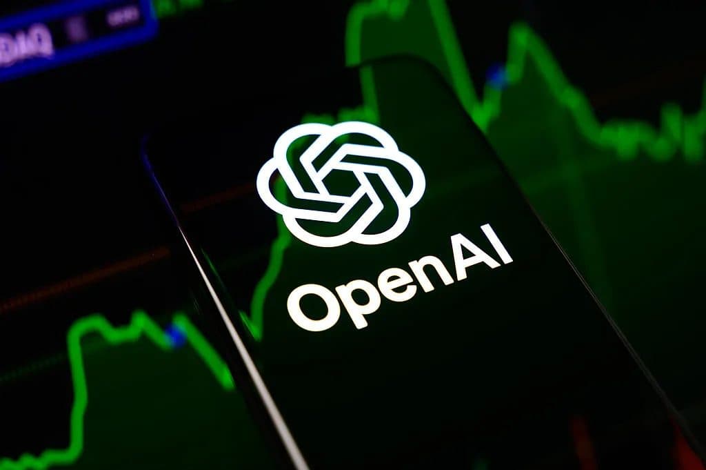 O logotipo da OpenAI em uma tela de celular diante de um painel com gráficos de mercado verdes