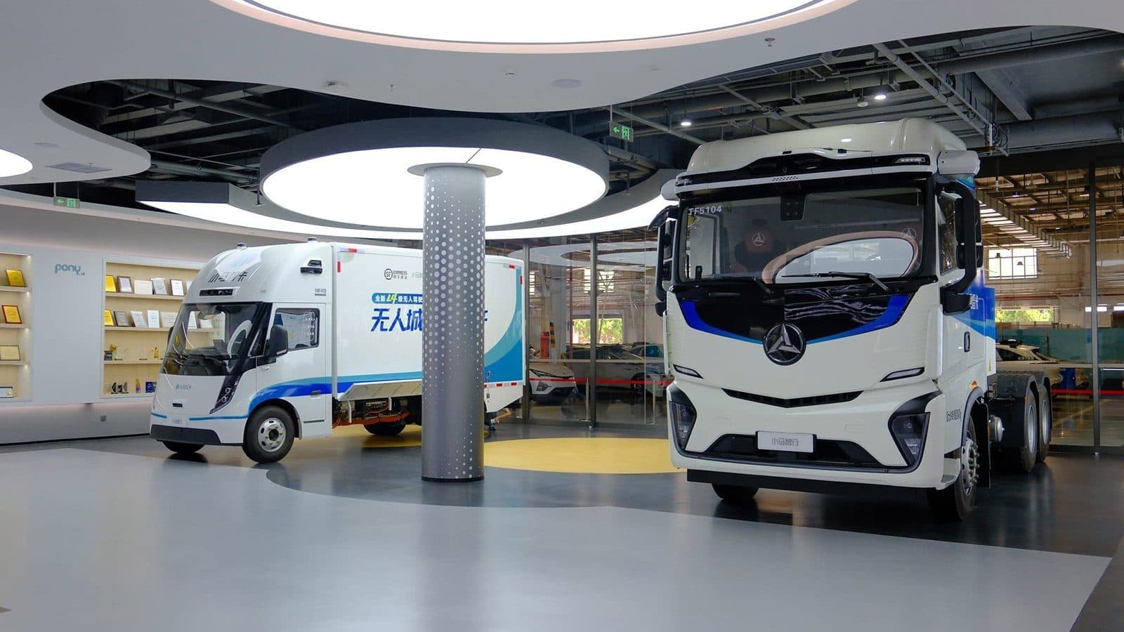 Two heavy trucks parked in a brightly lit indoor showroom