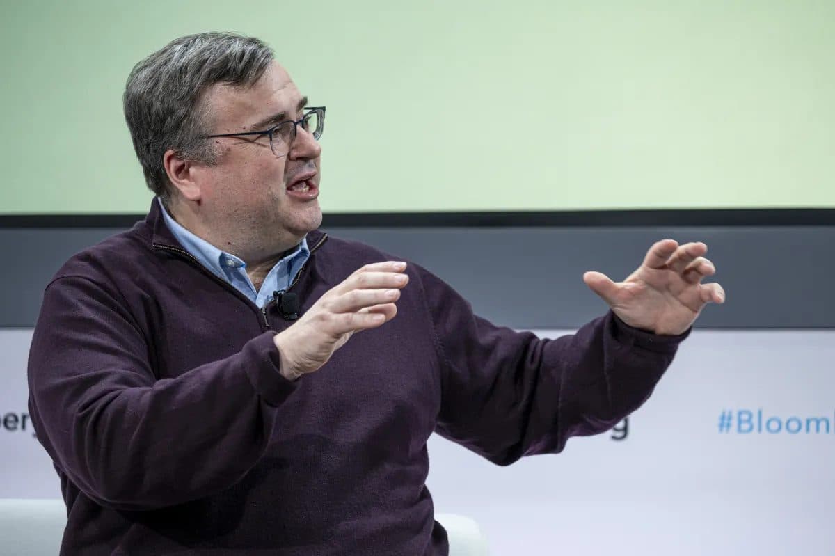 Reid Hoffman gesticulando com as duas mãos enquanto fala no palco, em frente a um fundo com a marca Bloomberg