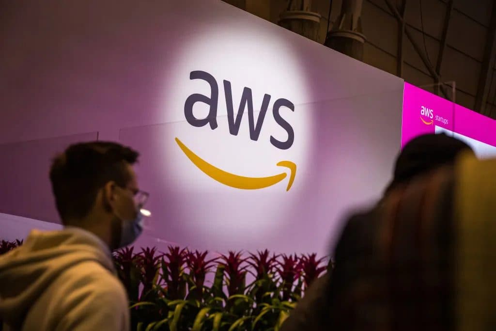 Visitors walking past a large illuminated AWS logo mounted on a wall at an Amazon Web Services event