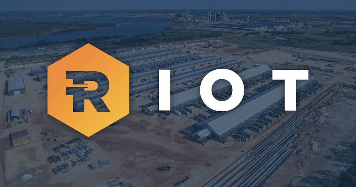 Il logo di Riot Platforms sopra una foto aerea del sito dell'azienda a Rockdale, Texas, con file di edifici visibili sotto.