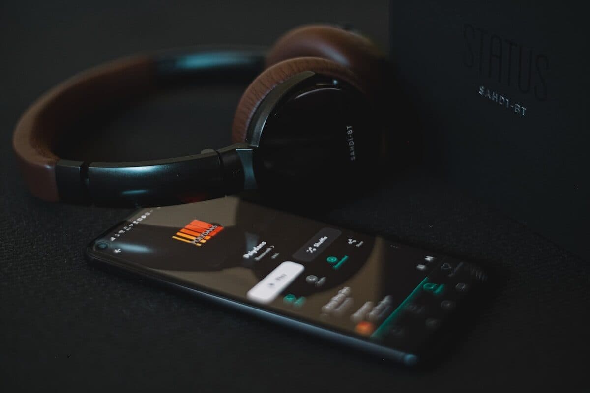 Over-ear headphones resting beside a smartphone showing a music player on a dark surface