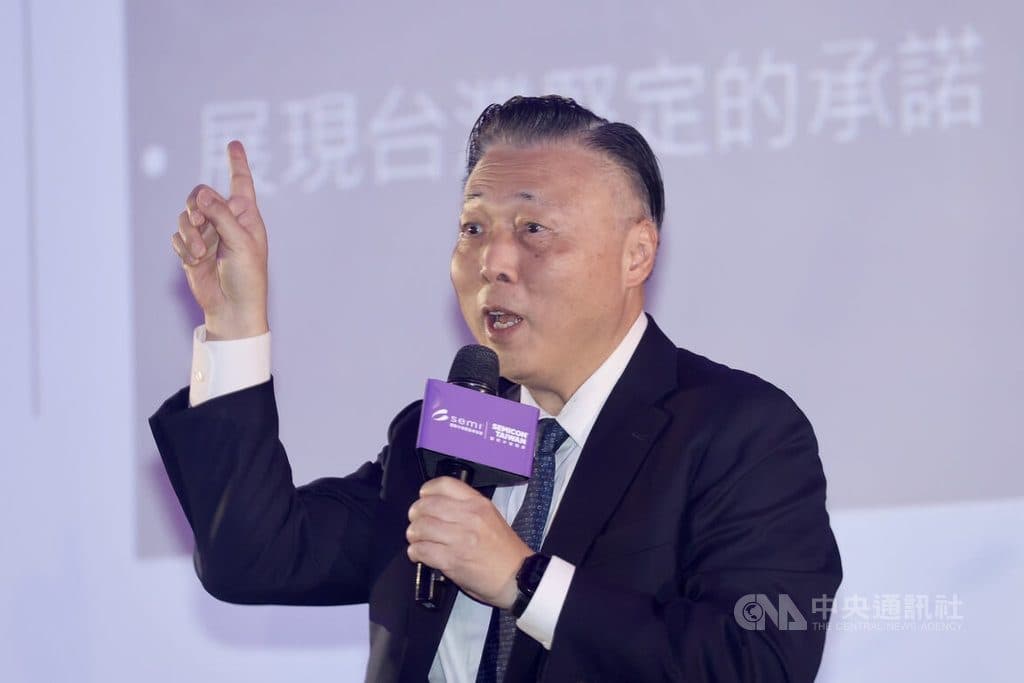 Un uomo in abito scuro parla in un microfono portatile durante un evento del settore a Taiwan, con watermark dell’agenzia di stampa CNA