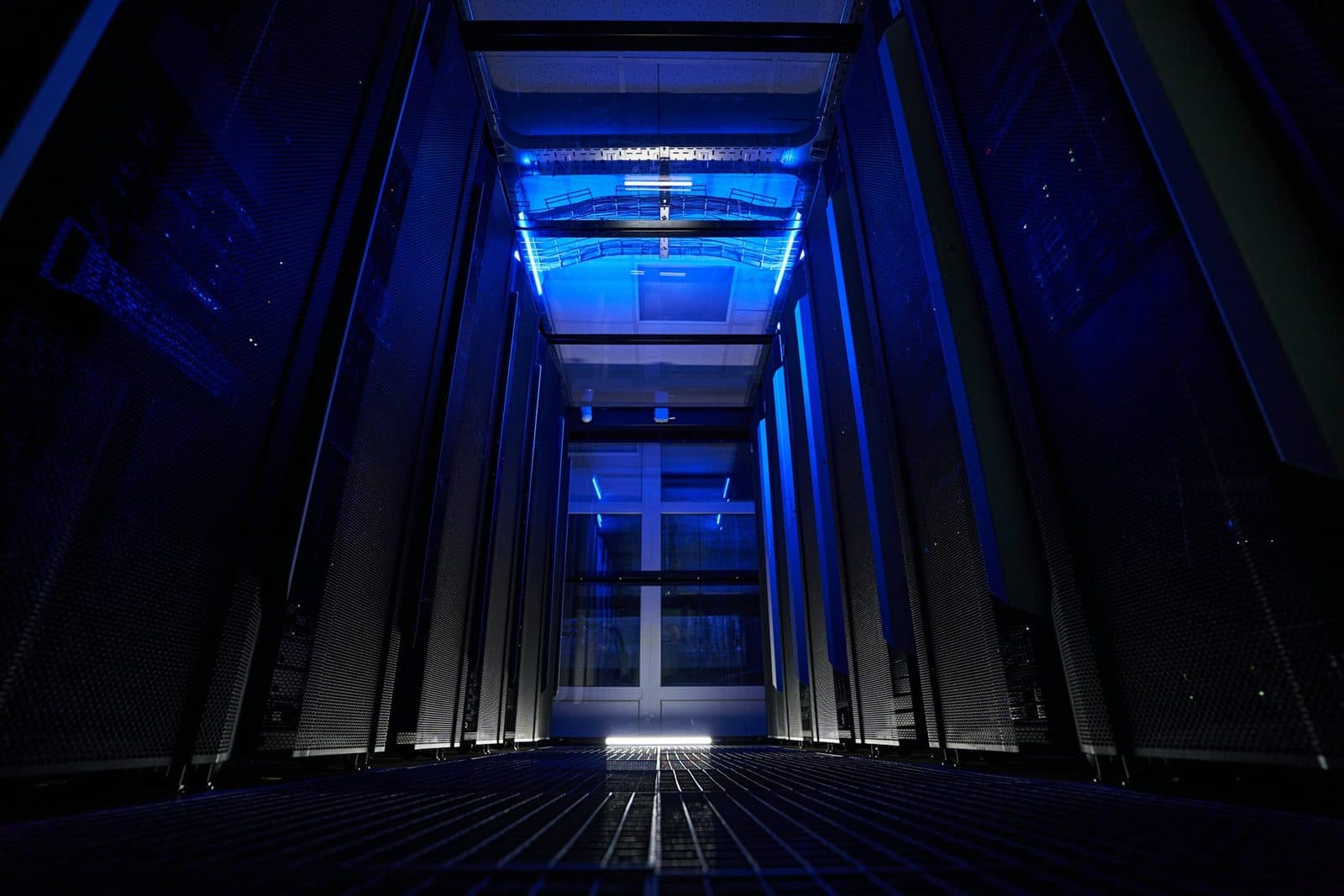 Un corridoio di data center illuminato di blu, con file di rack server scuri che si allontanano verso un punto di fuga.