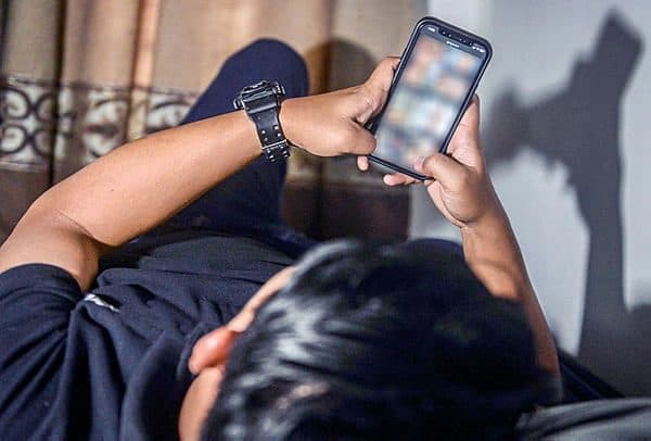 A person lying down, looking at a smartphone screen.