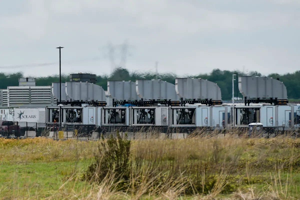 A row of grey containerised gas turbines standing in a green field