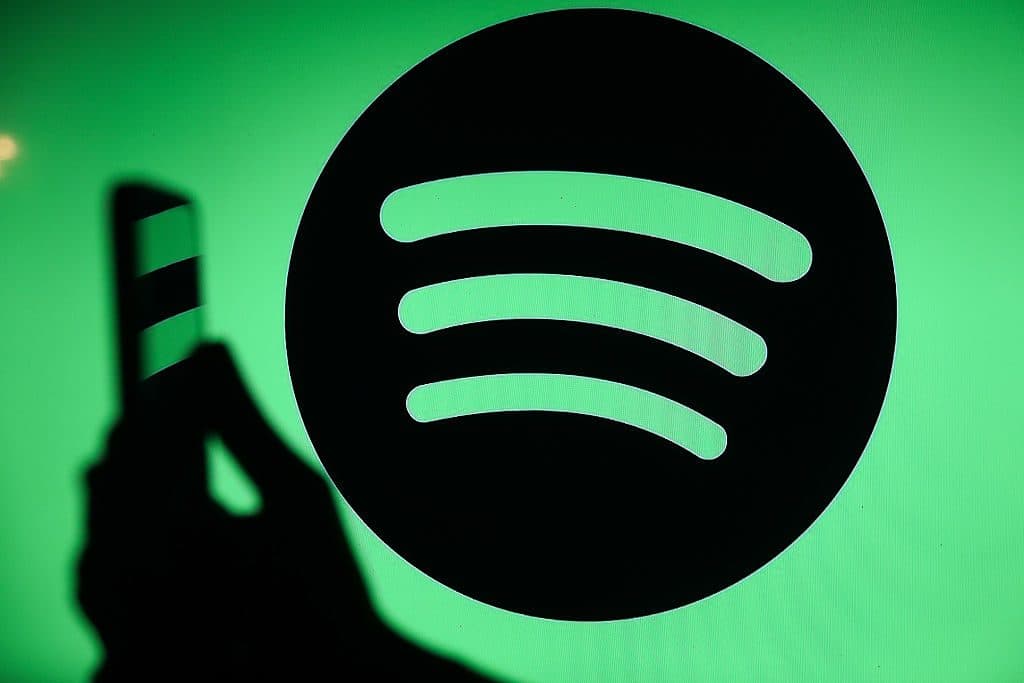 La sagoma di una mano che regge uno smartphone davanti a un grande logo Spotify proiettato su uno sfondo verde.