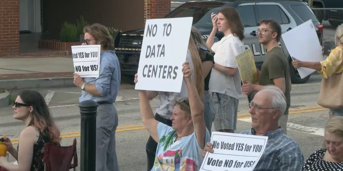 야외에 선 주민들이 "NO TO DATA CENTERS"와 "We Voted YES for YOU, Vote NO for US"라고 적힌 피켓을 들고 있다.