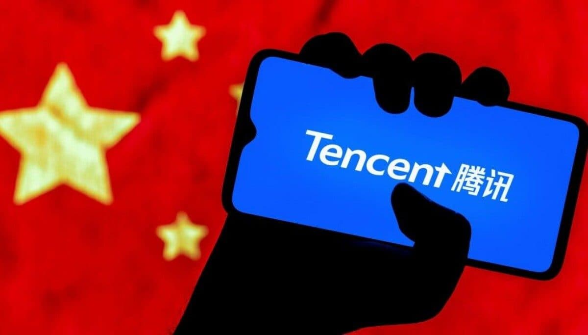 Una mano in siluette che tiene uno smartphone con il logo blu di Tencent, su sfondo rosso con le stelle gialle della bandiera cinese.