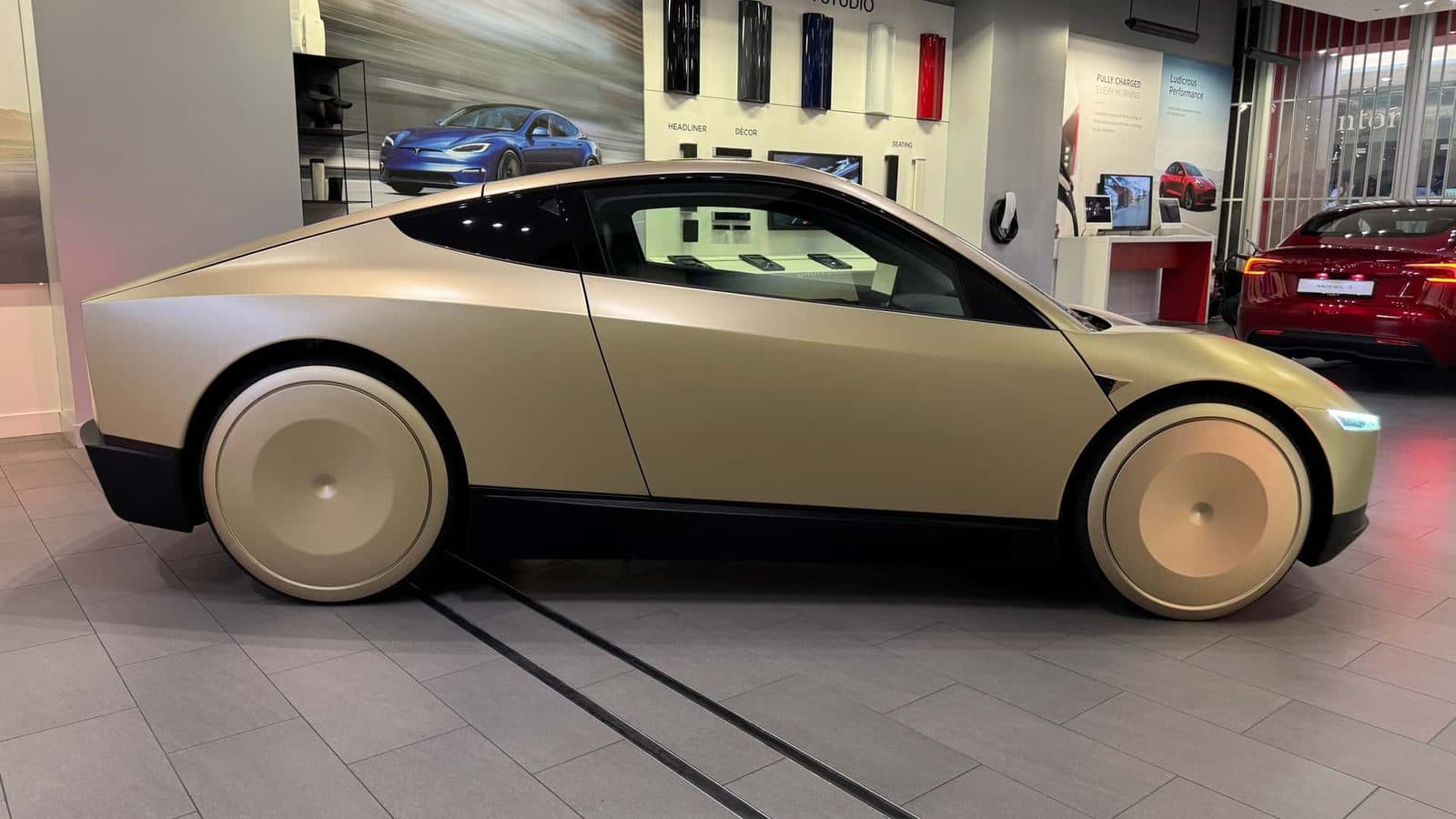 Un Tesla Cybercab dorato a due porte, privo di volante e pedali, fotografato al chiuso in uno spazio espositivo
