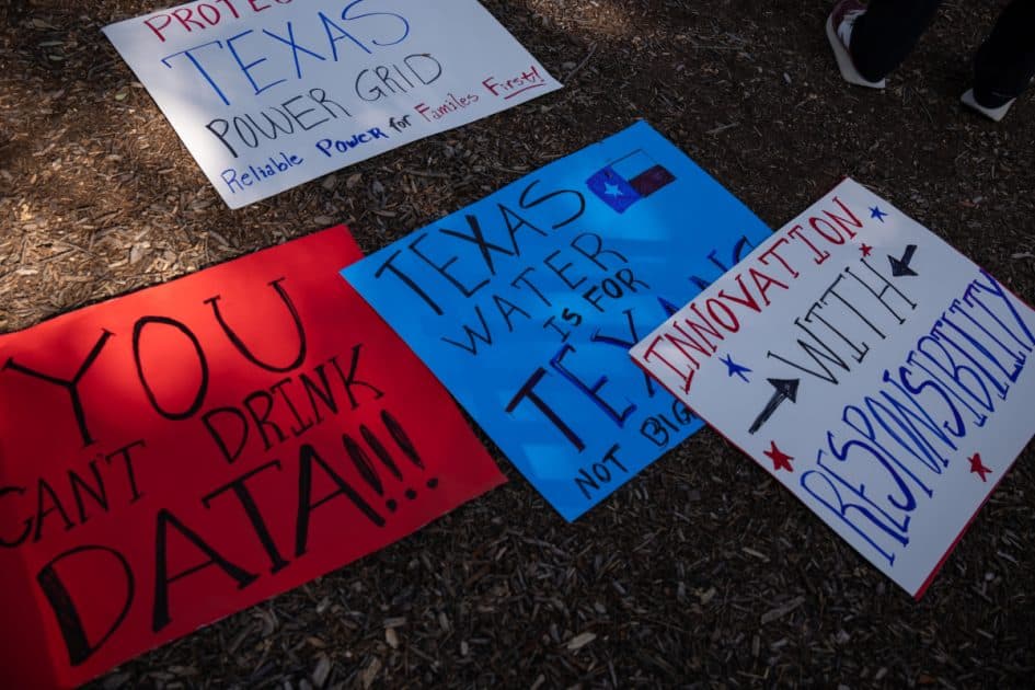 Cartelli di protesta scritti a mano, lasciati a terra, con le frasi “You can’t drink data!!!”, “Texas water is for Texans” e “Innovation with responsibility”.