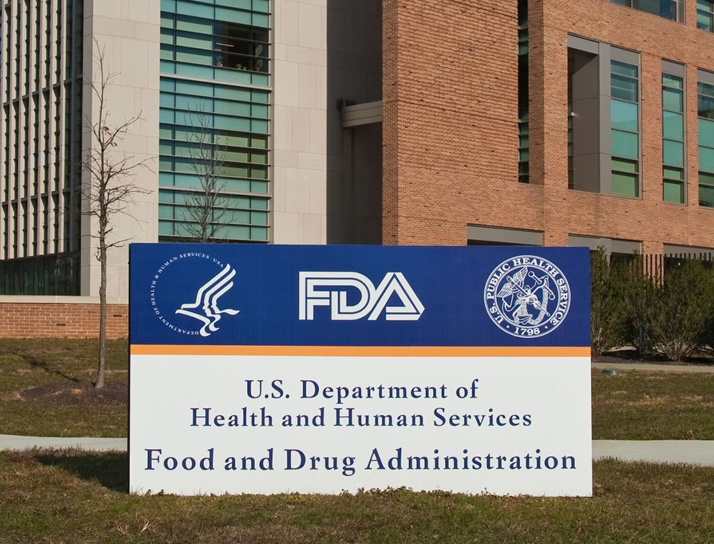 اللافتة الزرقاء والبيضاء خارج حرم US Food and Drug Administration، وتقرأ "U.S. Department of Health and Human Services, Food and Drug Administration"، مع مبنى مكاتب في الخلف.