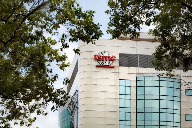 The curved glass facade of a TSMC building, seen through tree branches.