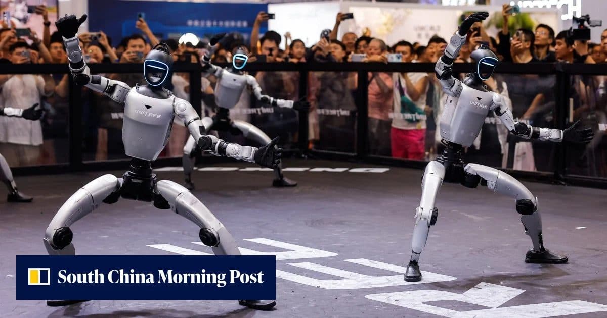 Dois robôs humanoides em postura agachada dentro de uma arena, com uma multidão de espectadores atrás de uma barreira; uma faixa do South China Morning Post aparece na parte inferior.