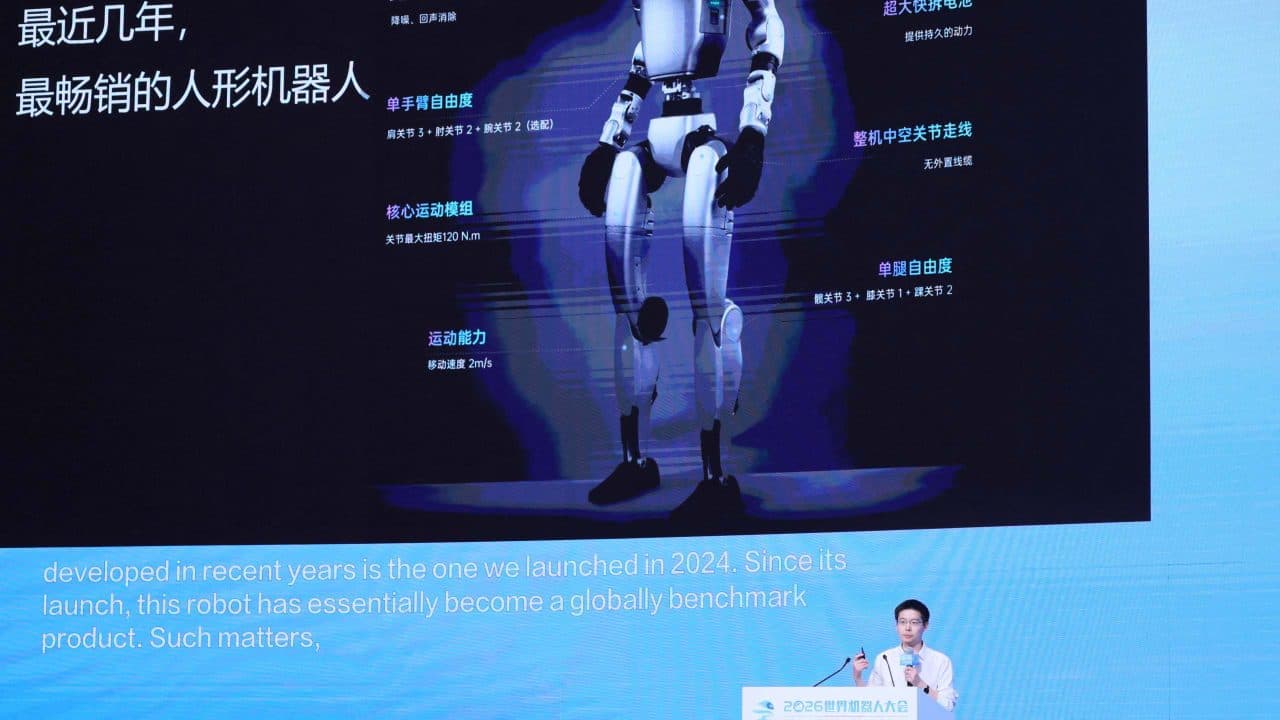Um painel de palco de conferência mostrando um robô humanoide com painéis de anotação em chinês ao lado, com um palestrante em um púlpito em primeiro plano.