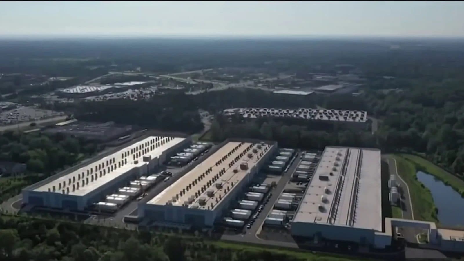 Veduta aerea di un campus di data center: file di edifici lunghi, bassi e senza finestre con unità di raffreddamento sul tetto, circondati da boschi e acqua.