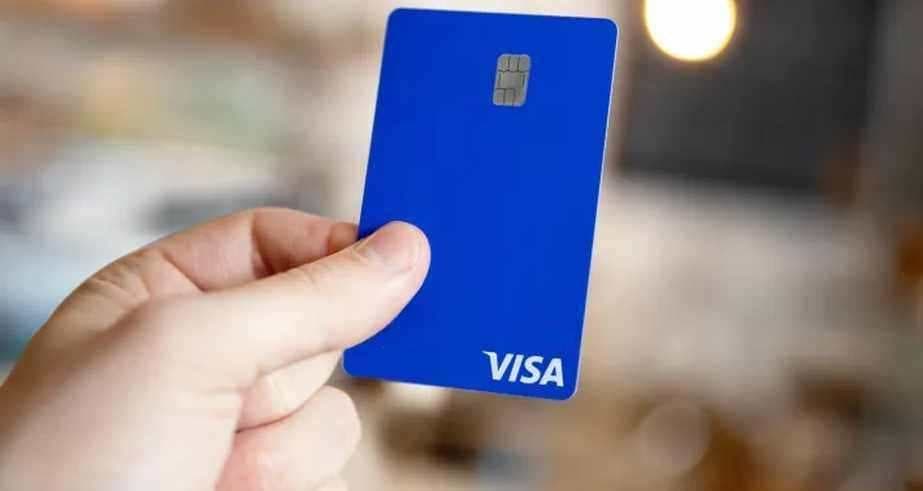 파란색 Visa 결제 카드를 카메라 쪽으로 든 손, 배경은 흐릿하게 처리됨
