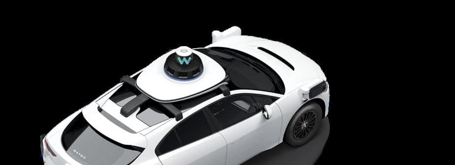 Un robotaxi Waymo bianco fotografato dall'alto su sfondo nero, con la cupola dei sensori sul tetto ben visibile.