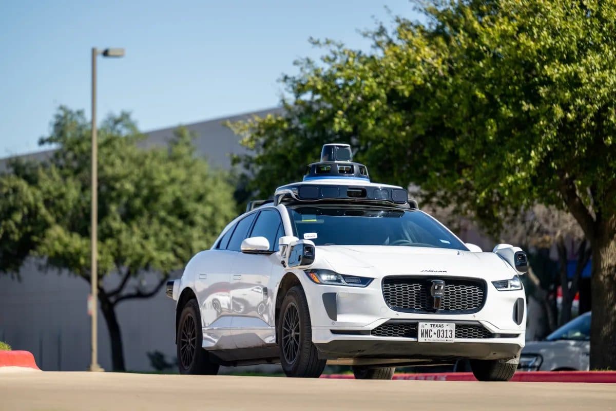 지붕에 센서가 장착된 흰색 Waymo Jaguar I-Pace 로보택시가 도로변에 주차돼 있다.