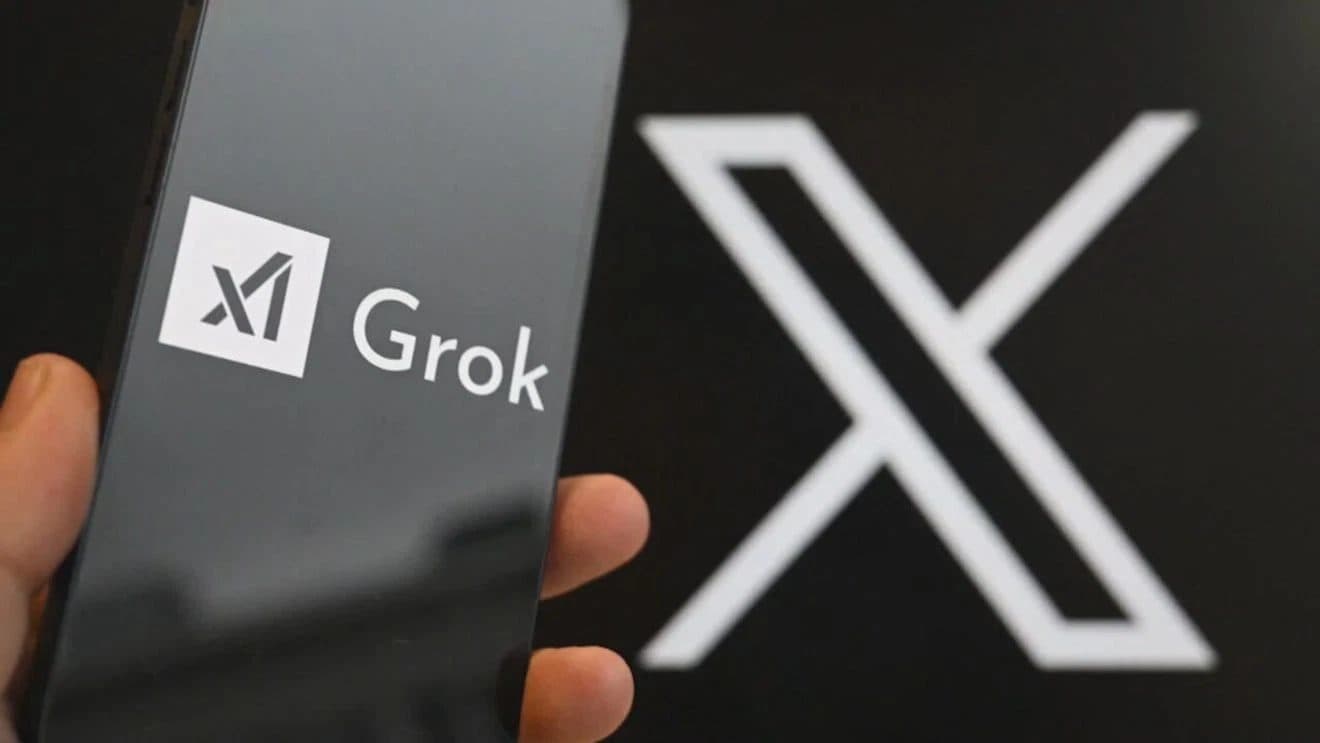 A phone showing the xAI Grok app, held in front of a large X logo.