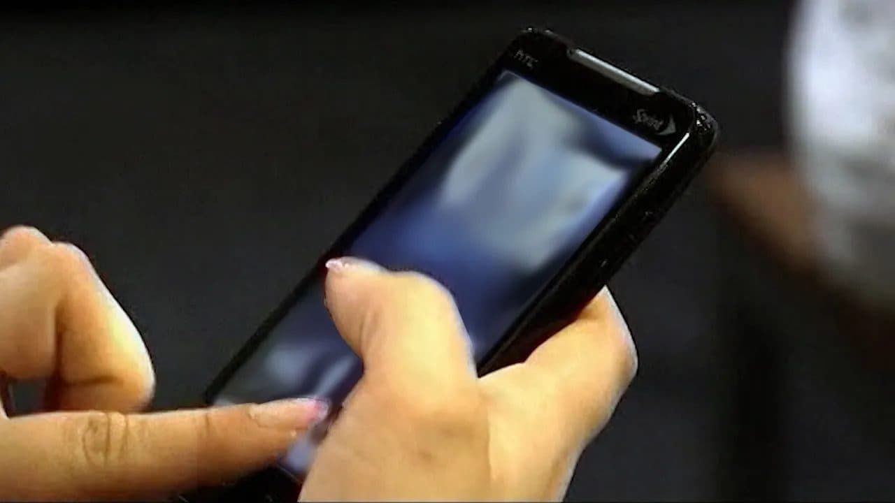 A file photograph of a person's hands holding a smartphone in low light, the screen turned away from the camera